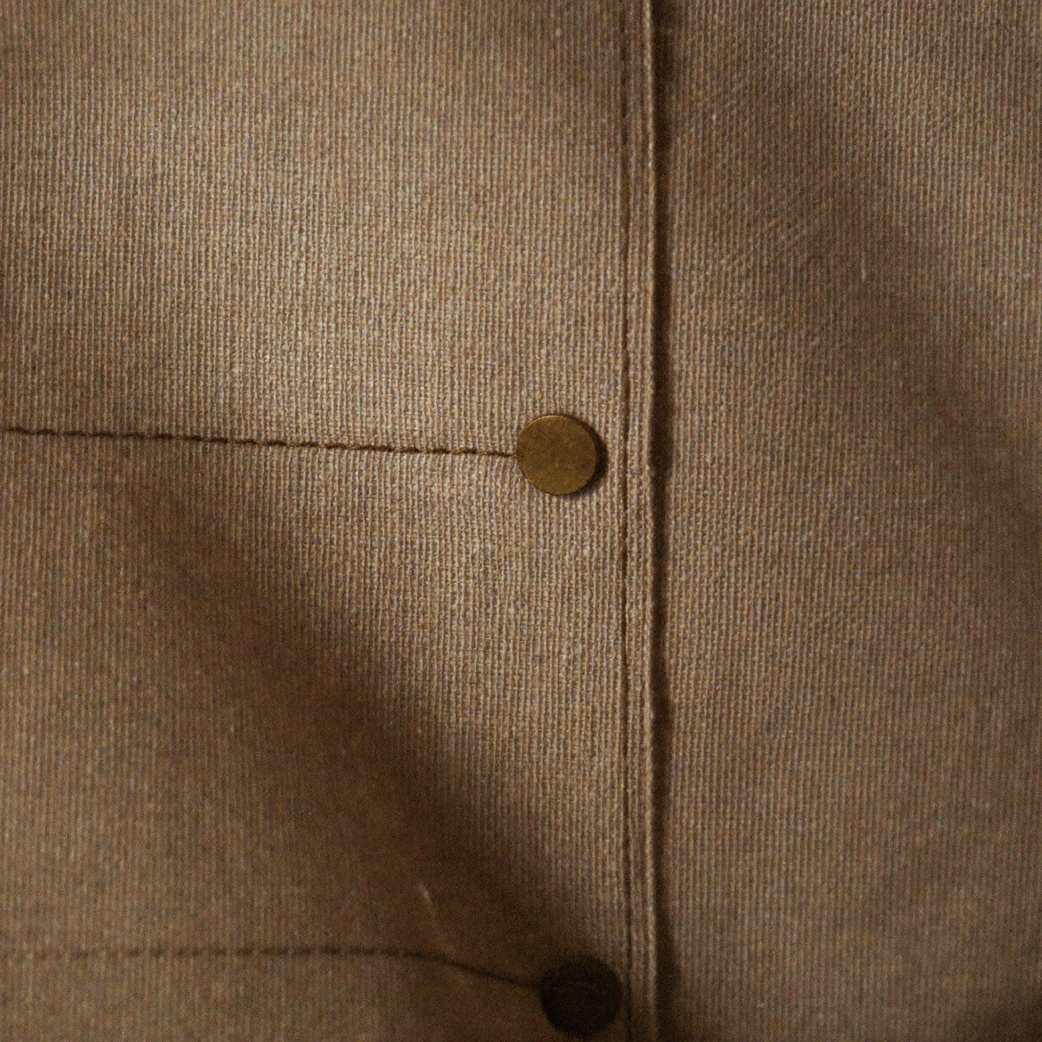 Close-up of heavyweight cotton duck canvas showing the weave, topstitching and a brass rivet
